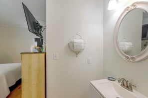 A hotel room with a bed, a desk with a computer, a wall-mounted light fixture, a mirror, and a bathroom with a sink and faucet. - Walk to Pope Park: Quaint Sylvester Studio (Sylvester)