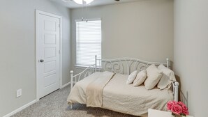 A bedroom with a white bed, a ceiling fan, a window with blinds, and a door. - Family-Friendly Fort Worth Home: Private Yard (Fort Worth)