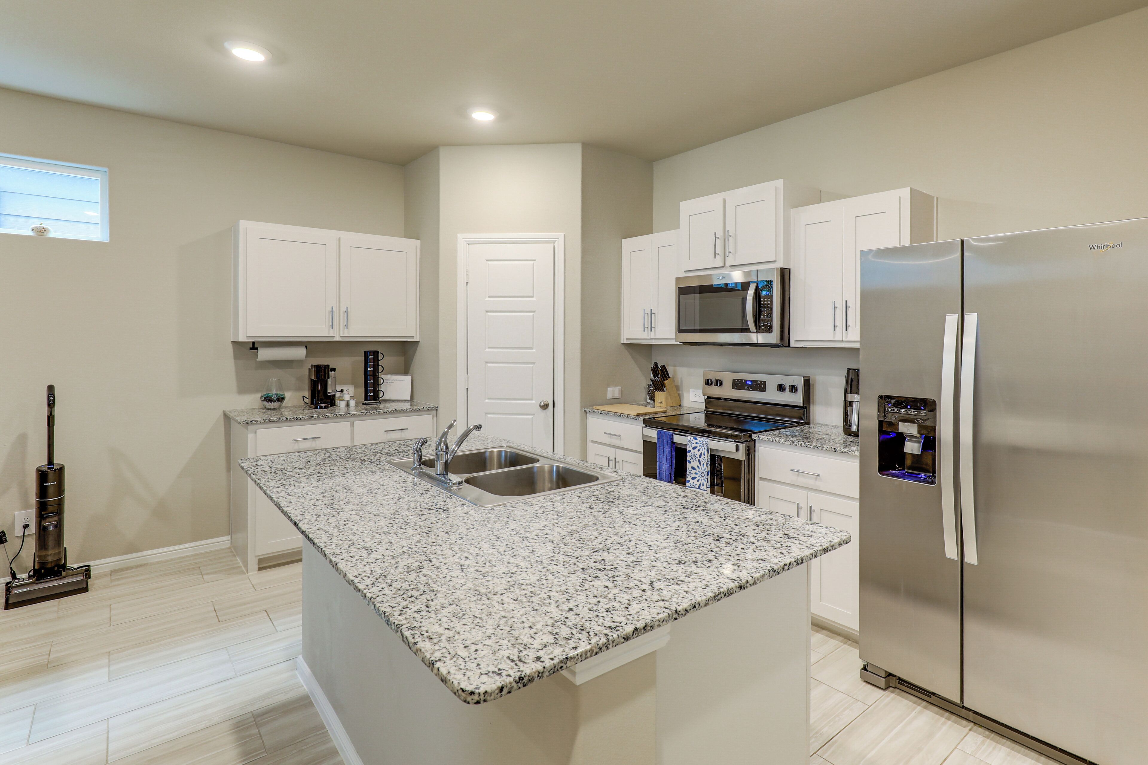 A modern kitchen with a granite countertop, stainless steel appliances, and white cabinetry.