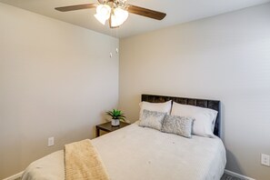 Una camera da letto con un letto, un comodino con una pianta e una ventola a soffitto.