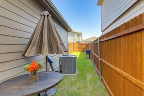 Ein Garten mit einer Terrasse, einem Grill und einem Holzzaun.