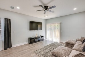 A modern living room with a flat-screen TV, a ceiling fan, and a large window with blinds. - 3 Mi to Dtwn & EverBank Stadium! Family Townhome (Jacksonville)