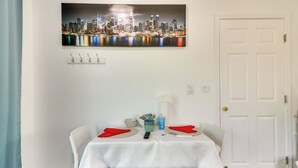 A dining area with a table set for two, a cityscape painting above, and a white door to the right. - Soaking Tub, Fire Pit! Hemet Studio Suite (Hemet)