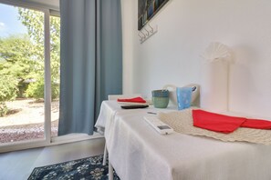 Ein Zimmer mit einem Bett, einem Tisch mit Fernbedienung, einem roten Stoff und Blick auf Grün.