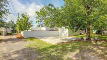 A residential area with a paved driveway, a white fence, and a large tree.