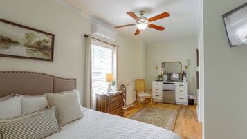 A bedroom with a bed, a ceiling fan, a dresser, a chair, and a desk.