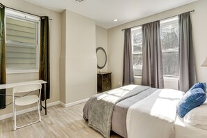 Une chambre à coucher avec un lit, un bureau, une chaise, une commode et une fenêtre avec des rideaux.