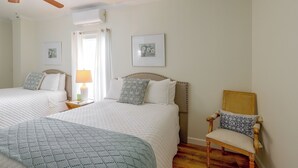 A hotel room with two beds, a chair, a ceiling fan, and artwork on the walls.