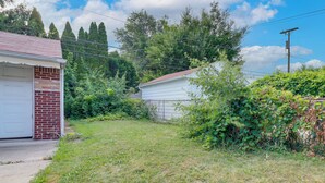 A residential property with a garage, a brick wall, and a grassy yard. - 8 Mi to Dtwn Detroit! Apt w/ Shared Yard (Dearborn)