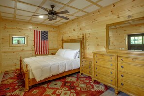 A wooden cabin bedroom with a bed, dresser, and ceiling fan.