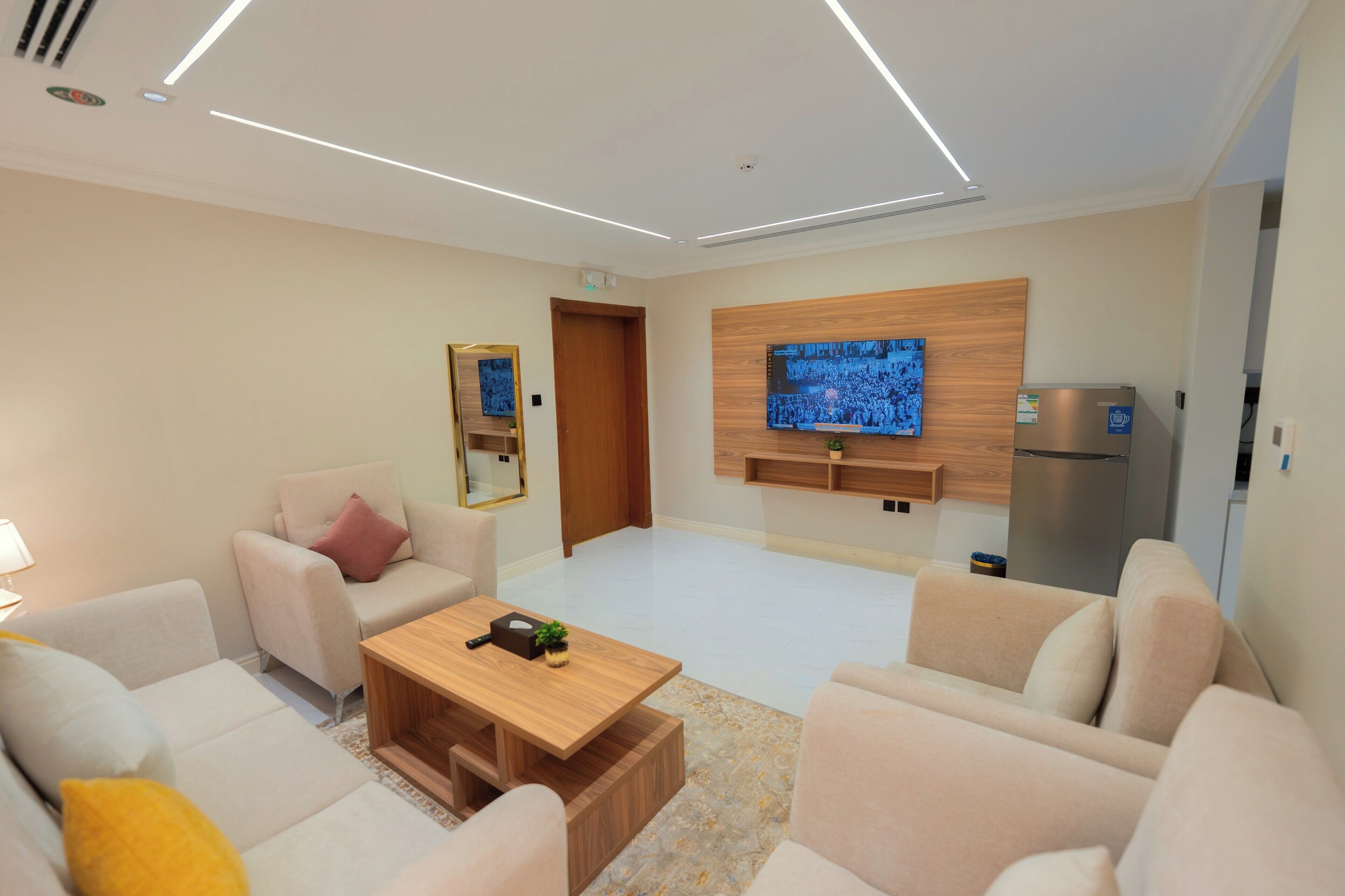 Una sala moderna con un conjunto de sofás, una mesa de centro, un televisor de pantalla plana montado en la pared y un refrigerador empotrado.
