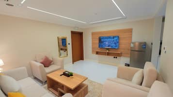 Una sala moderna con un conjunto de sofás, una mesa de centro, un televisor de pantalla plana montado en la pared y un refrigerador empotrado.