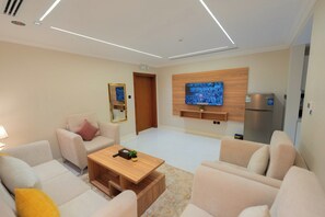 Una sala moderna con un conjunto de sofás, una mesa de centro, un televisor de pantalla plana montado en la pared y un refrigerador empotrado.