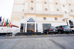 A building with a grand entrance, multiple flags, and parked cars. - Viola Al- Asalah (Dammam)