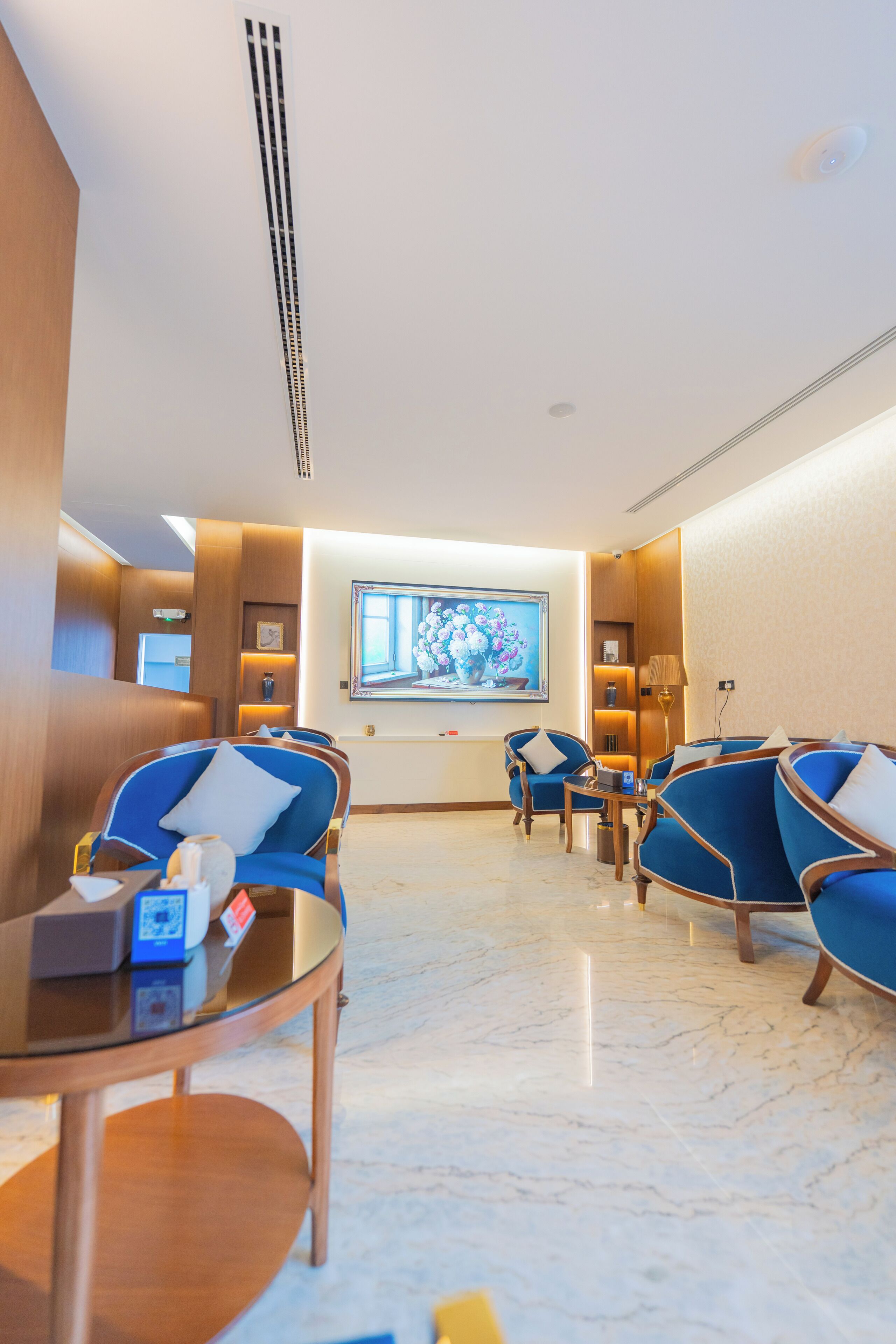 A hotel lobby with seating areas, a television screen, and a marble floor.