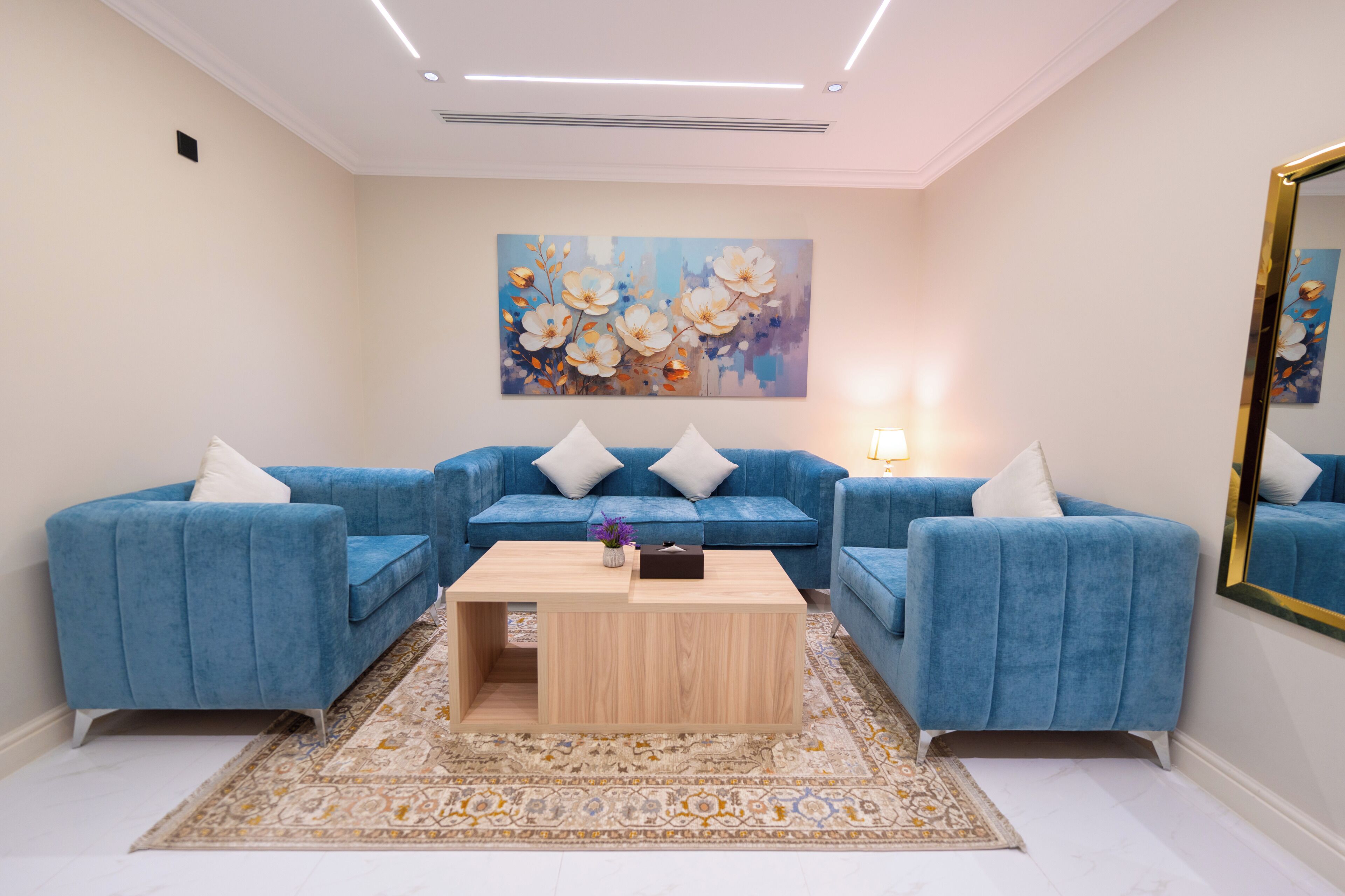 Una sala de estar con un sofá seccional azul, una mesa de centro de madera y un cuadro grande con motivos florales en la pared.