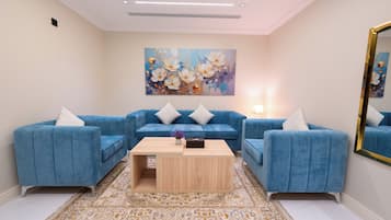Una sala de estar con un sofá seccional azul, una mesa de centro de madera y un cuadro grande con motivos florales en la pared.