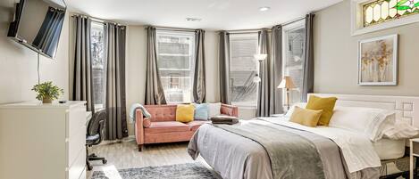 Une chambre moderne avec un lit, un bureau, une chaise, une télévision et une fenêtre avec des rideaux.