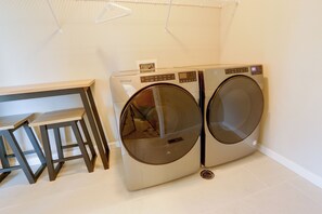 A laundry room with two front-loading Whirlpool washers, a wooden table, and a metal drying rack. - Extended Stay In Fort Collins! Townhome w/ Gym (Fort Collins)