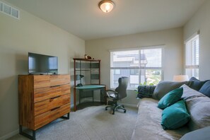 A room with a wooden dresser, a desk with a chair, a television on the dresser, a window with blinds, and a couch with pillows. - Extended Stay In Fort Collins! Townhome w/ Gym (Fort Collins)