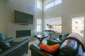 A modern living room with a fireplace, a mounted TV, and a dining table with a horse sculpture. - Extended Stay In Fort Collins! Townhome w/ Gym (Fort Collins)