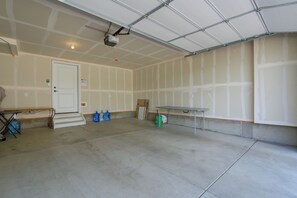 En rummelig, ufuldstændig garage med en hvid dør, et arbejdsbord og diverse byggematerialer.