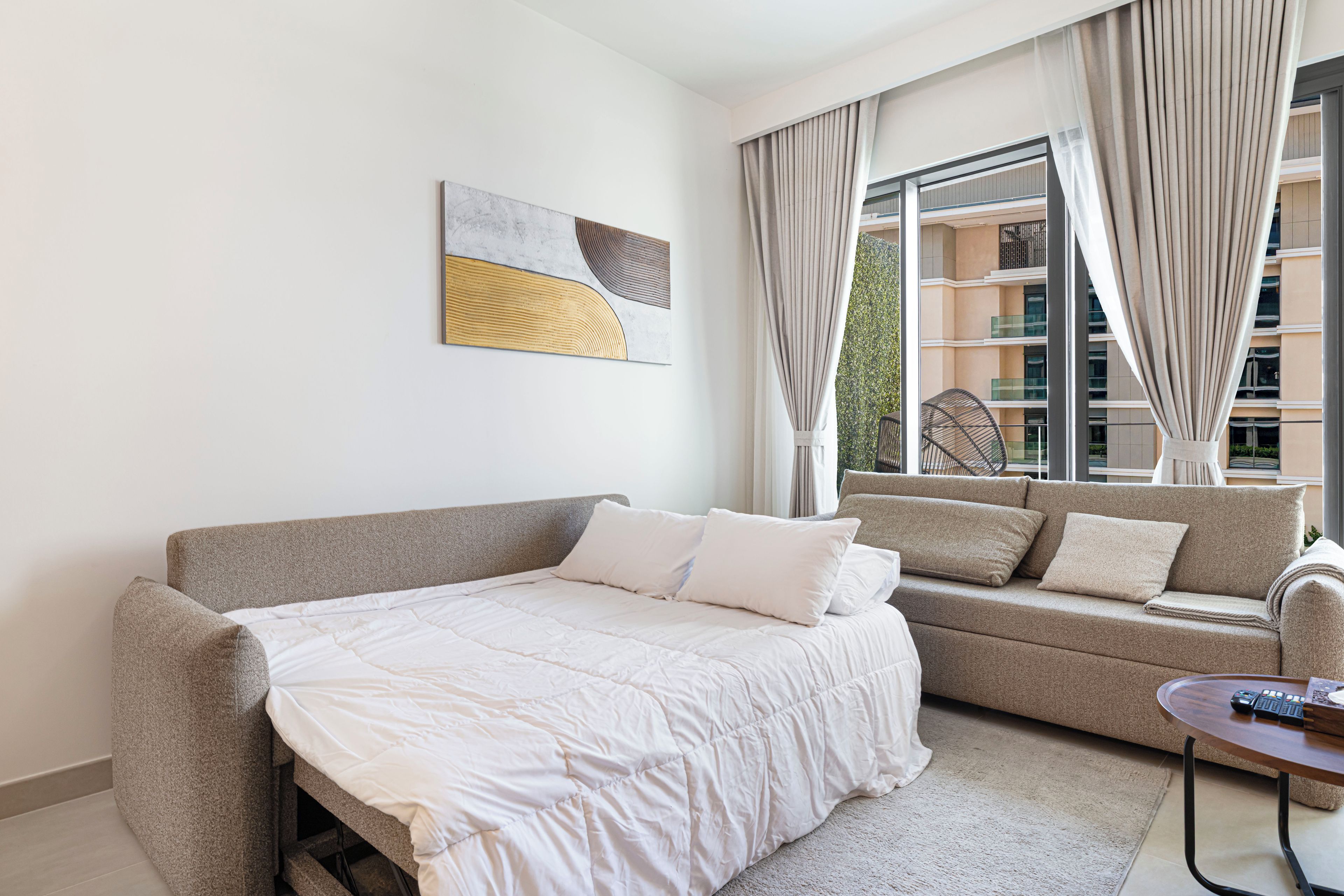 Una habitación de hotel moderna con una cama grande, un sofá, una mesita y vistas al exterior del edificio.