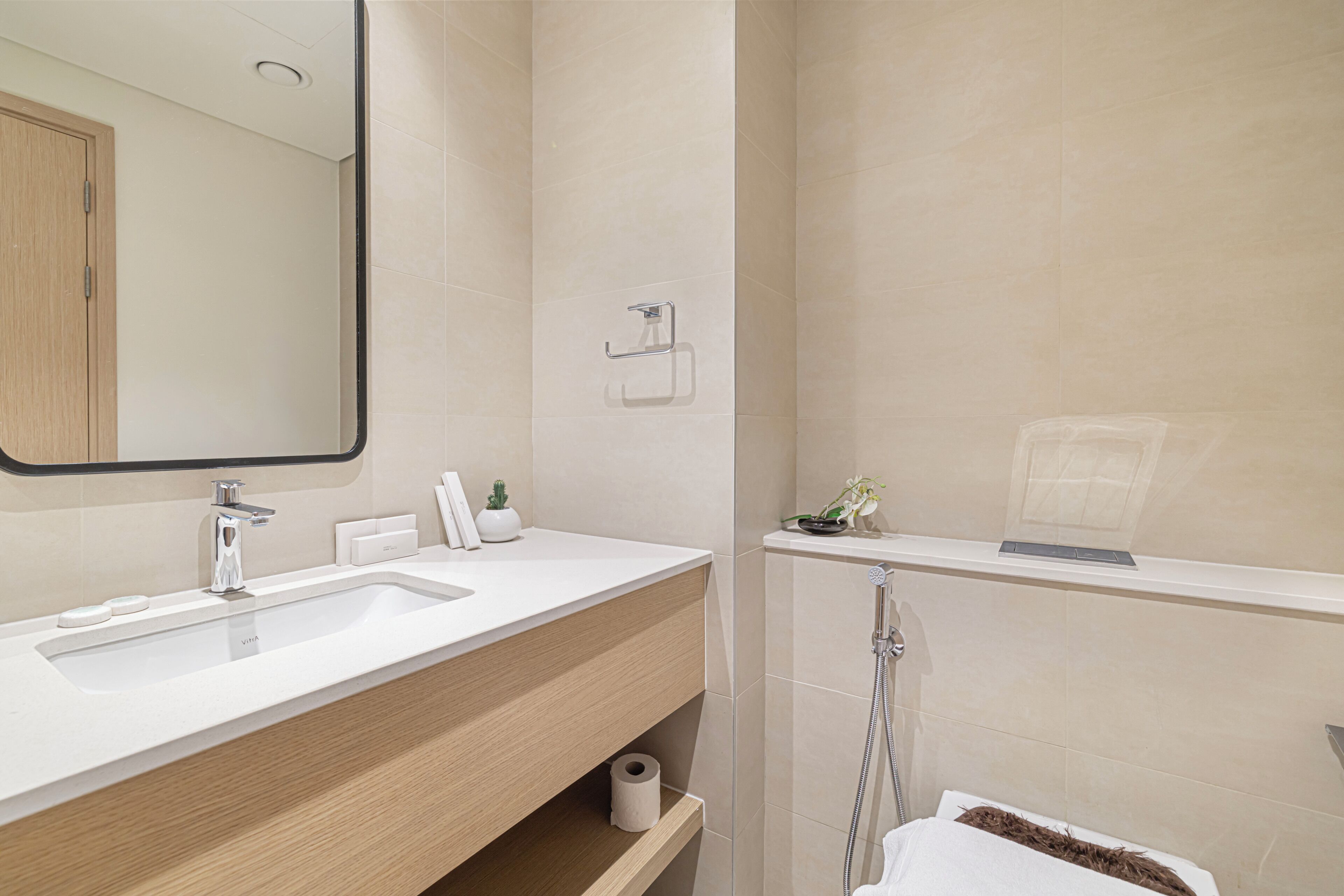 A modern bathroom with a white sink, a mirror, a towel rack, and a shower area.