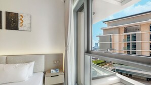 Une chambre d’hôtel avec un lit, une table de chevet, une fenêtre donnant sur un immeuble et une œuvre d’art murale.