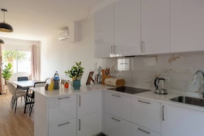 Eine moderne Küche mit weißen Schränken, ein Essbereich mit Tisch und Stühlen sowie ein Fenster mit Vorhängen.