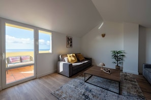 Ein modernes Wohnzimmer mit einer Couch, einem Couchtisch und Blick auf das Meer durch große Fenster.