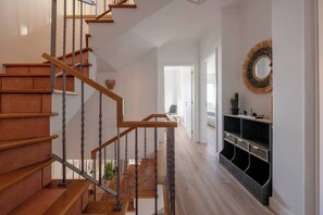 Eine Treppe mit Holzsitzstufen und Metallgeländern, die zu einem Flur mit einer schwarzen Konsole und einem Spiegel mit Fransenstickerei führt.