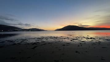 Uma praia com mar calmo, montanhas ao longe e um pôr do sol.