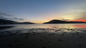 Uma praia com mar calmo, montanhas ao longe e um pôr do sol.