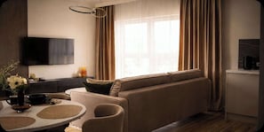 A modern living room with a sofa, a dining table with a vase of flowers, and a flat-screen TV mounted on the wall.