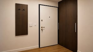 A room with a wooden floor, a white door with a black frame, a wooden wardrobe, and a wall-mounted light switch.