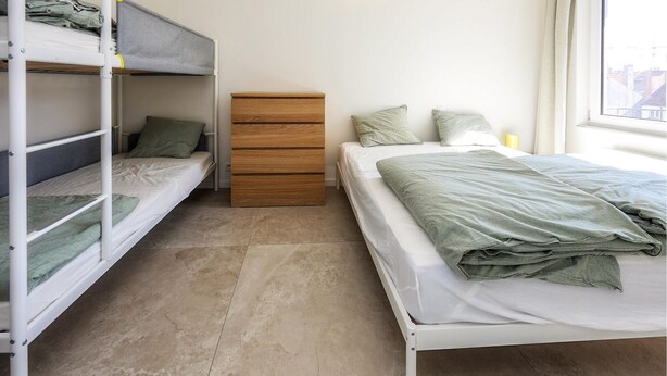 A dorm-style room with bunk beds, a wooden dresser, a single bed, and a window with a view. - 2 bedroom lovely apartment in Oostende (Oostende)