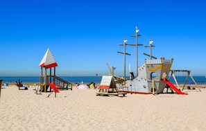Une plage avec un poste de surveillance pour les sauveteurs, un petit abri et une structure en bois avec un toboggan.