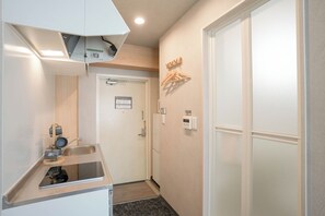 Una habitación de hotel con kitchenette, una puerta con un cartel y un termostato fijado a la pared.
