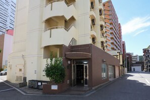 Un edificio de varios pisos con entrada a nivel de calle, un pequeño jardín y un balcón visible.
