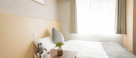 Une chambre d’hôtel avec un lit, une table de chevet avec un téléphone, un vase avec une plante et une fenêtre avec des rideaux.
