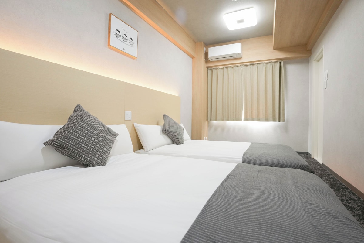 Ein Hotelzimmer mit zwei Betten, einem gerahmten Bild an der Wand, einer Klimaanlage und einem Fenster mit Vorhängen.