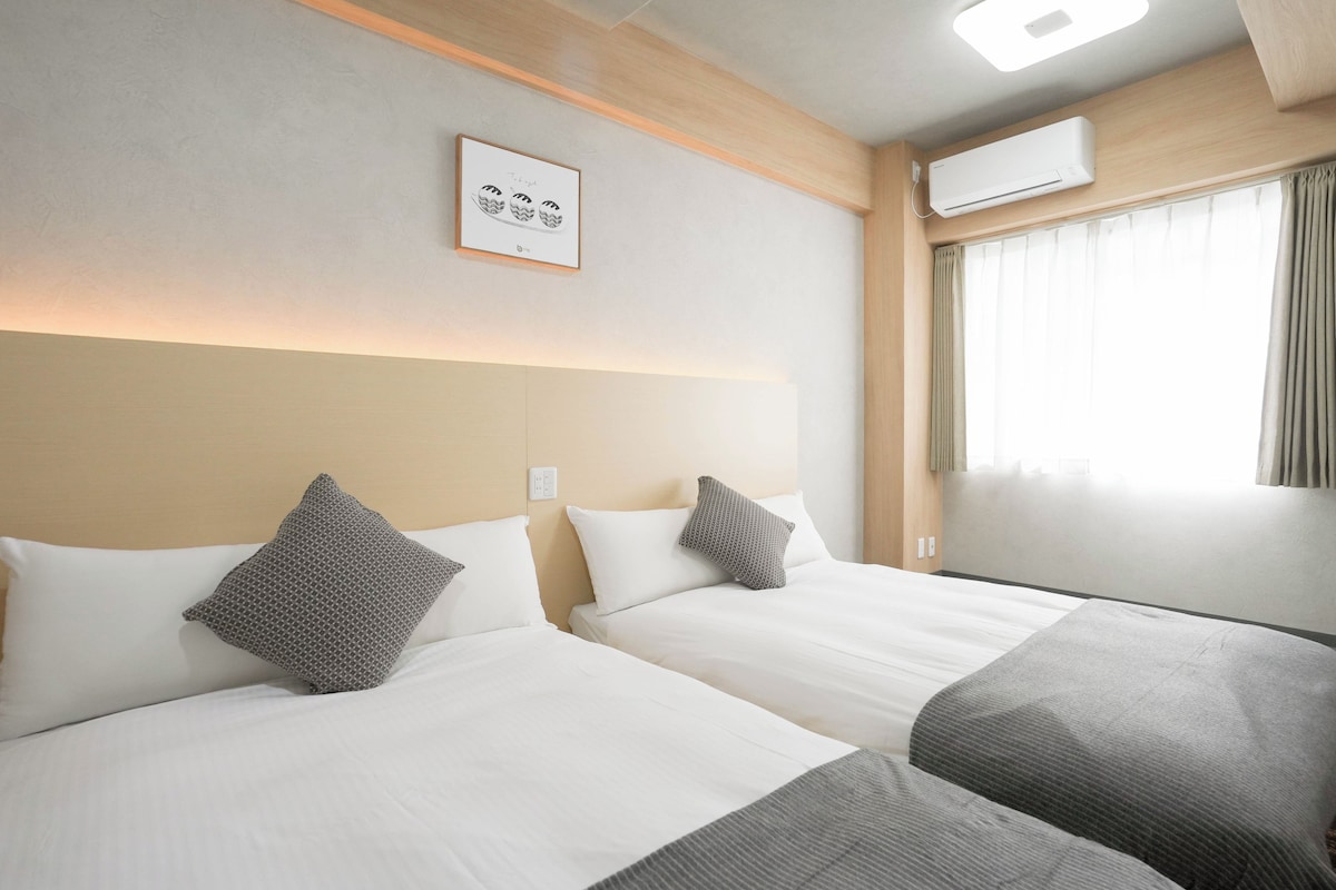 Habitación de hotel con dos camas, un cuadro en la pared, un equipo de aire acondicionado y una ventana con cortinas.