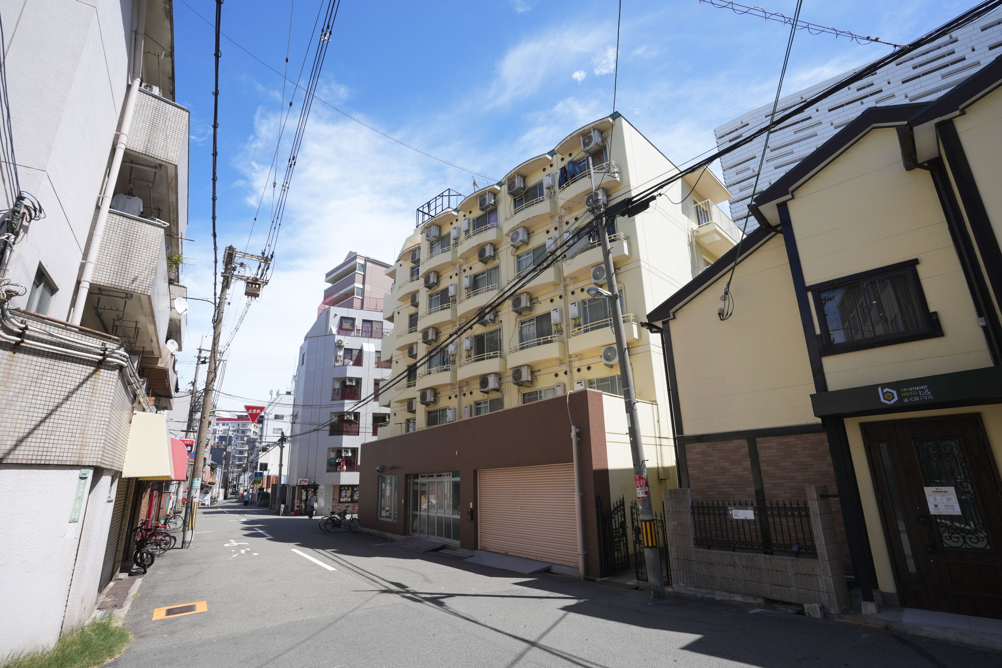 A narrow urban street lined with multi-story residential buildings, some with balconies and air conditioning units.