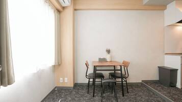 A small, modern room with a wooden table and four chairs, a small vase on the table, and a window with curtains.