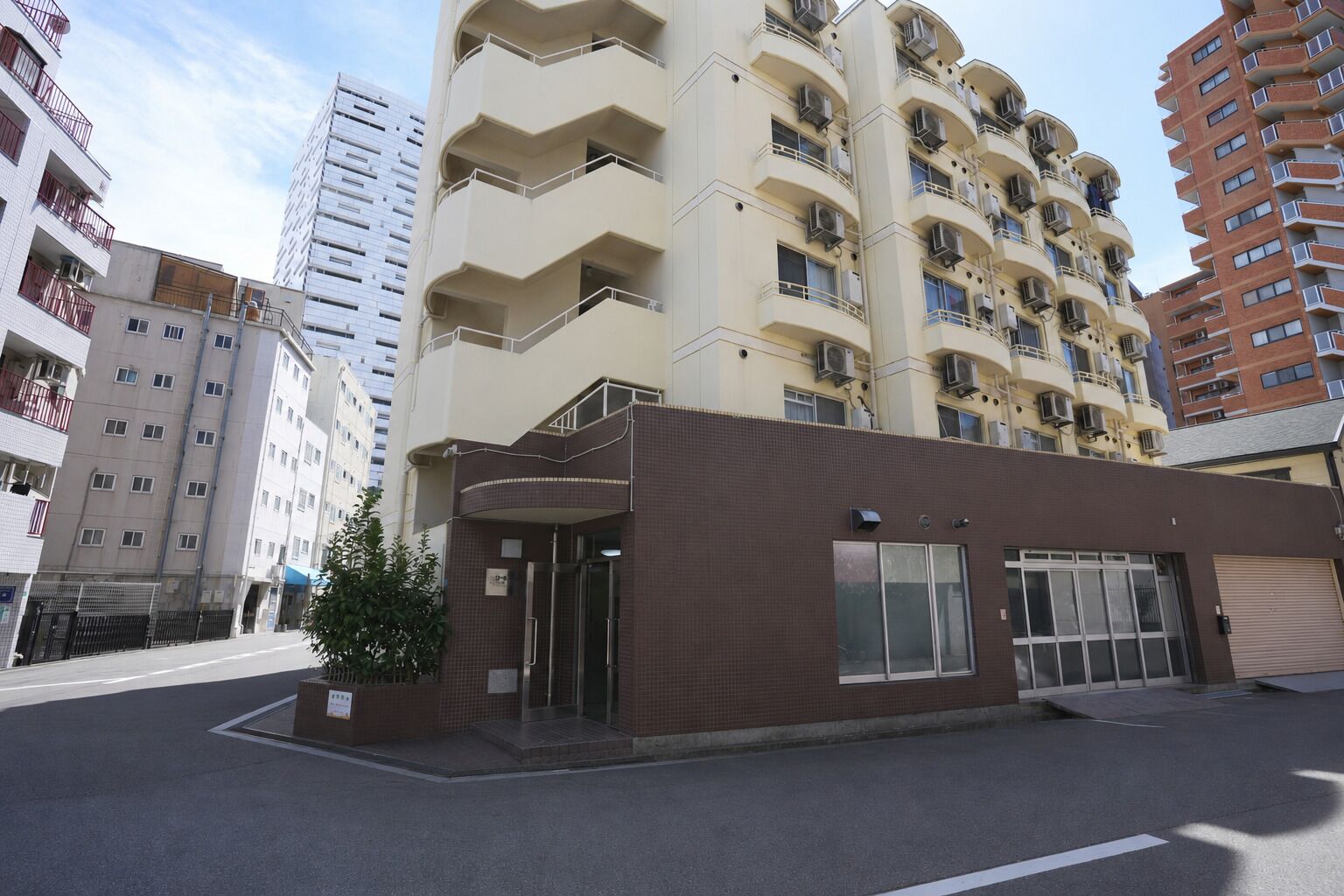 Un edificio de varios pisos con fachada plana, acceso a nivel de calle y una estructura adyacente pequeña con revestimiento de tejas marrones.