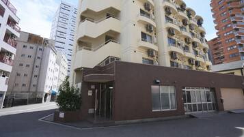 Un edificio de varios pisos con fachada plana, acceso a nivel de calle y una estructura adyacente pequeña con revestimiento de tejas marrones.