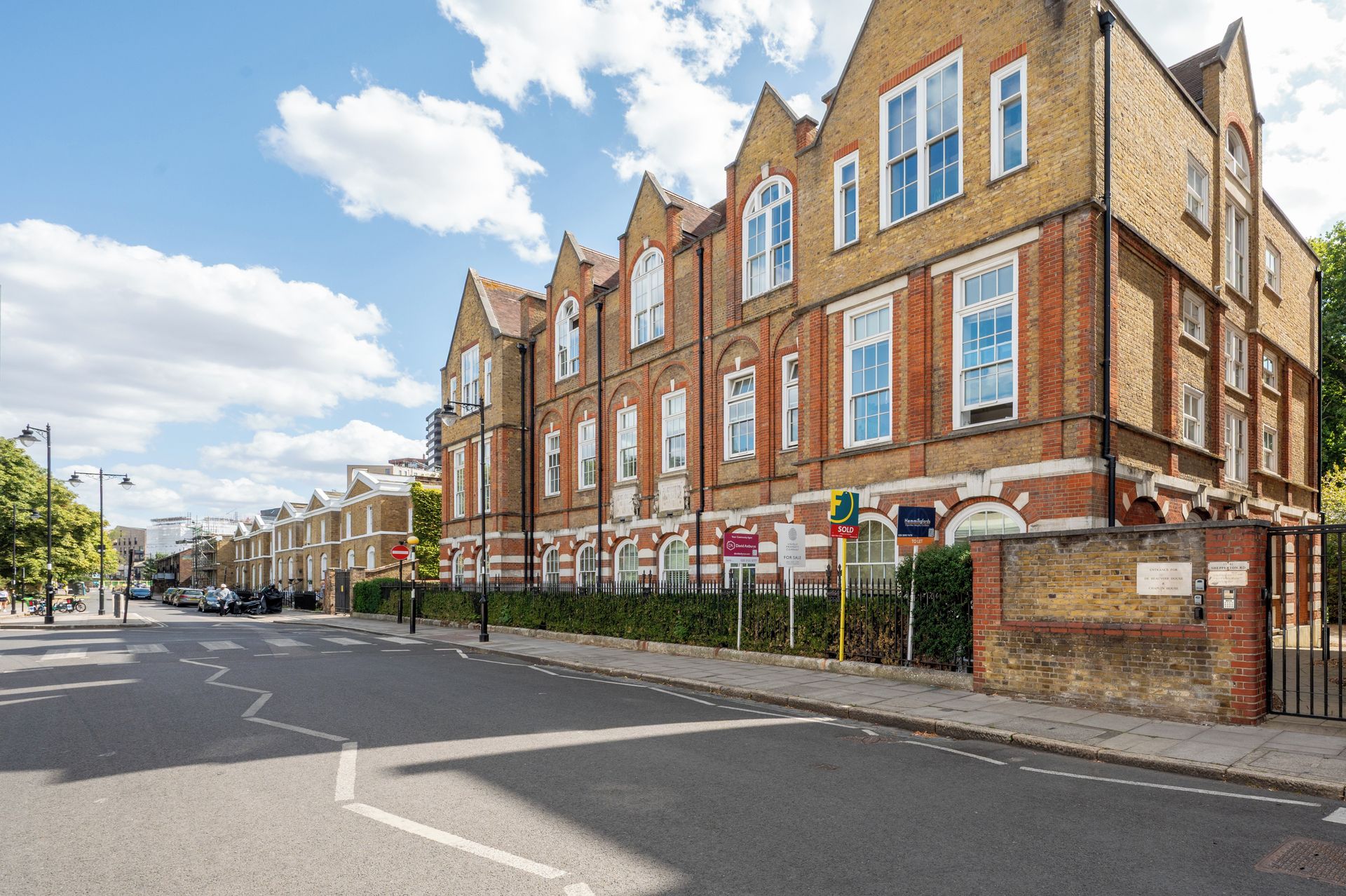 A row of red-brick terraced houses with white window frames, a clear sky, and a street with no visible traffic.