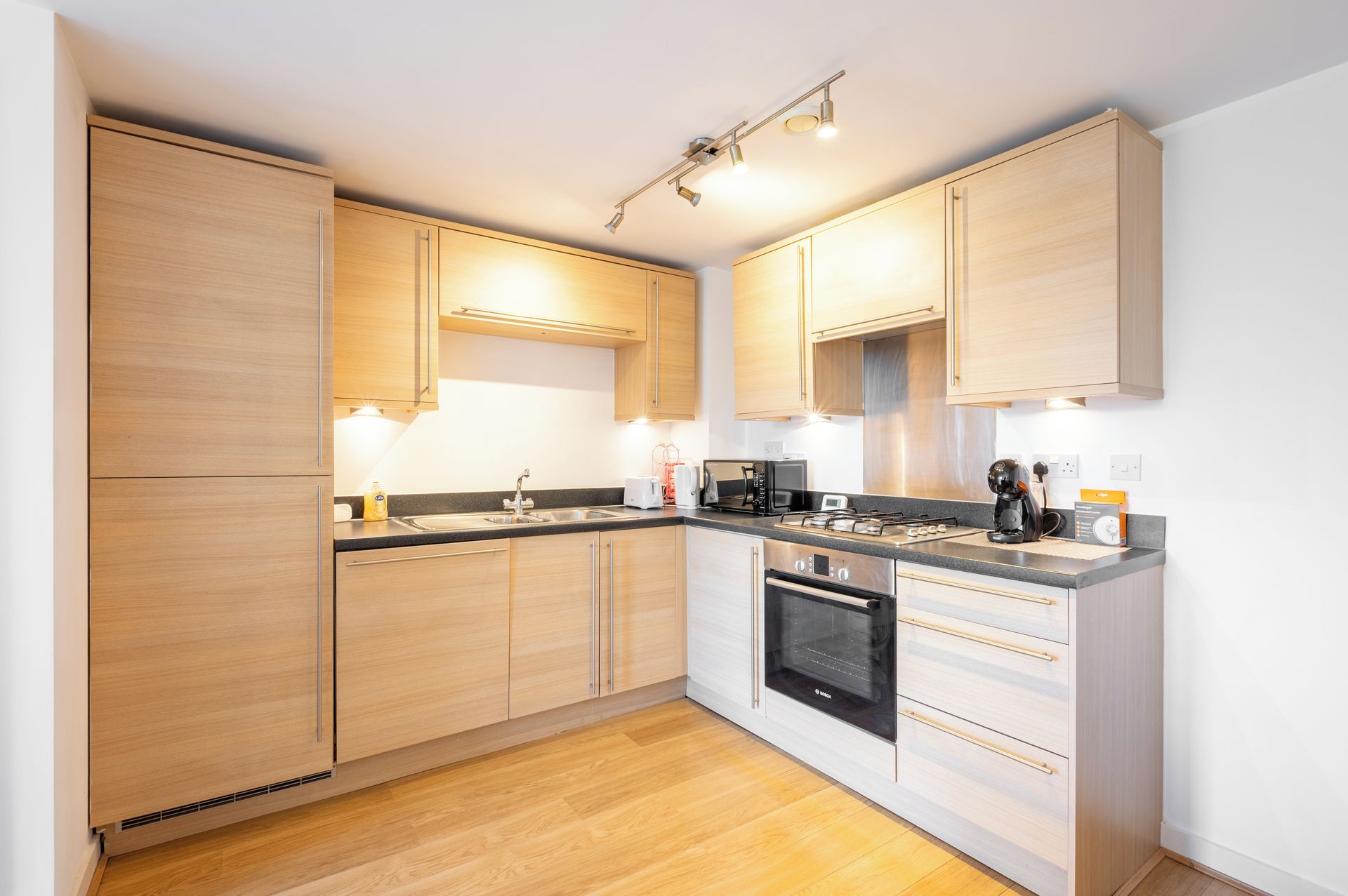 Une cuisine moderne avec des meubles en bois, un four encastré et un plan de travail équipé de divers appareils électroménagers.