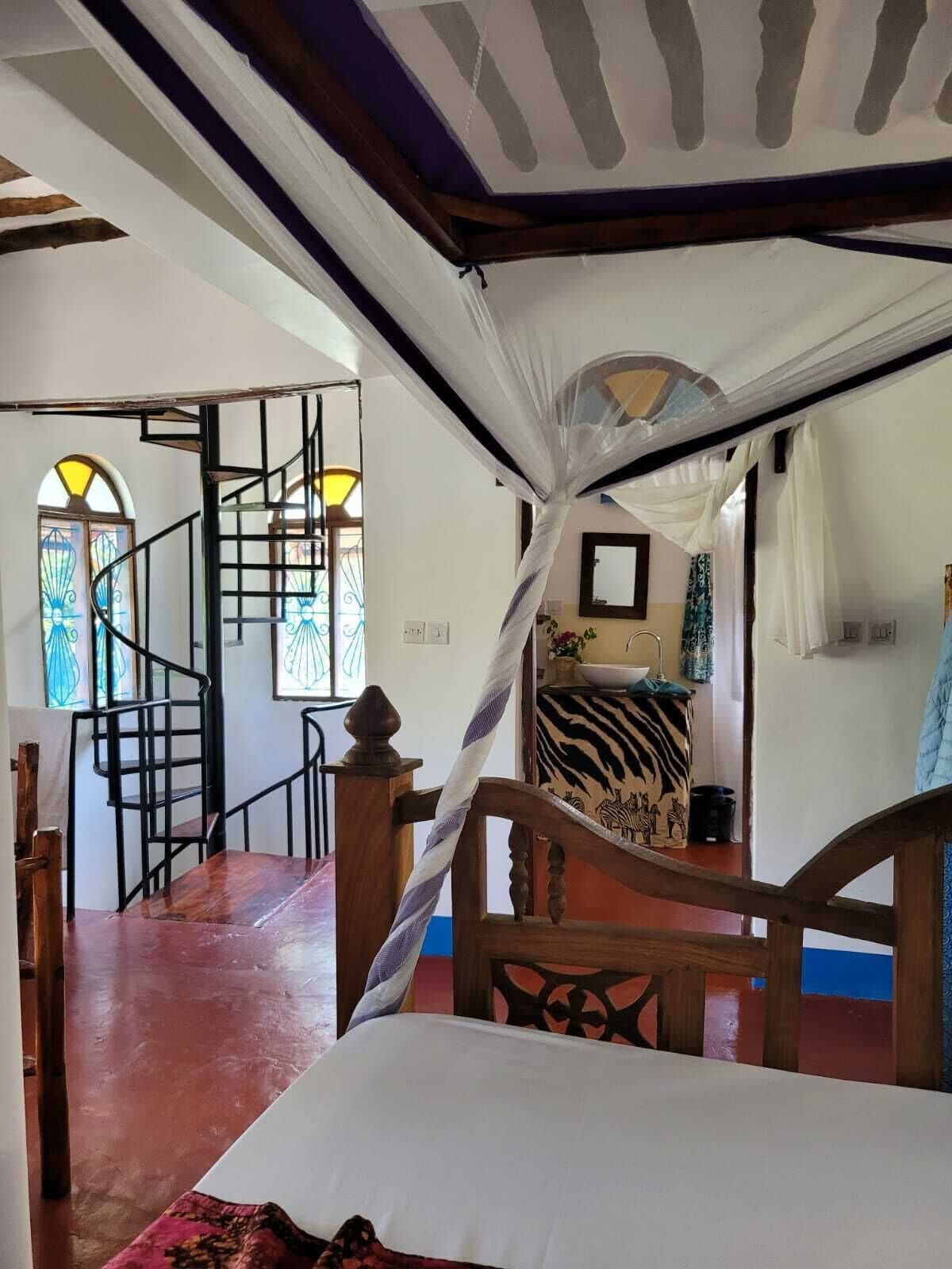 A bedroom with a canopy bed, a staircase, and a view of a room with a zebra-patterned bedspread.